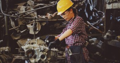 Woman Wears Yellow Hard Hat Holding Vehicle Part